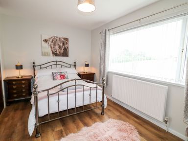 A bedroom with a metal bed frame bedside tables with lamps a large window and a pink rug on a wooden floor at Glebe Farm Cottage in Rathfriland County Down