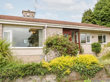 Front exterior of a single story house with large windows wooden door and garden plants at Glebe Farm Cottage in Rathfriland County Down