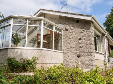 Exterior view of a stone and pebble dash house with a glass conservatory and garden at Glebe Farm Cottage in Rathfriland County Down