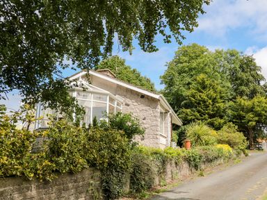 A stone house with a glass conservatory surrounded by bushes and trees at Glebe Farm Cottage in Rathfriland County Down