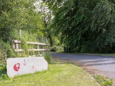 A roadside area with a wooden fence stone sign and trees at Glebe Farm Cottage in Rathfriland County Down
