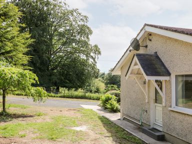 A side view of a house with a door and window next to a garden and trees at Glebe Farm Cottage in Rathfriland County Down