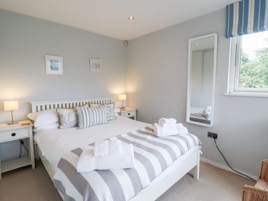 A bedroom with a white bed with striped blanket and pillows two bedside tables with lamps a window with striped blind and a mirror on the wall at 9 Cedars in St Agnes