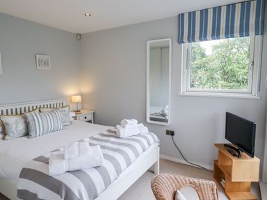 A bedroom with a bed a bedside table with a lamp a wall mirror a window a chair and a TV on a wooden stand at 9 Cedars in St Agnes