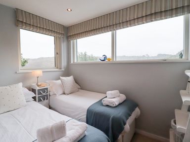 A bedroom with two single beds bedside table and windows with striped blinds at 9 Cedars in St Agnes