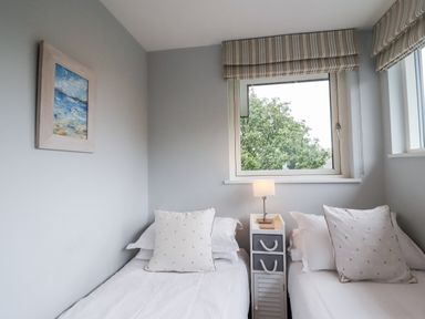 A bedroom with two single beds a bedside table and a window with a view of trees at 9 Cedars in St Agnes