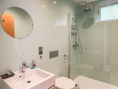 A bathroom with a sink a circular mirror a toilet and a shower area at 9 Cedars in St Agnes