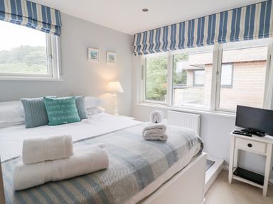 A bedroom with a bed with pillows and folded towels next to two windows with striped blinds at 9 Cedars in St Agnes