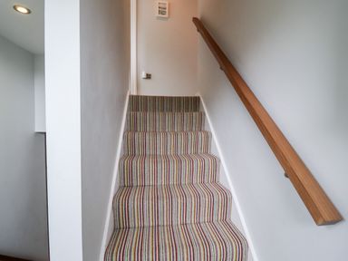 A stairway with striped carpet and a wooden handrail on the right wall at 9 Cedars in St Agnes