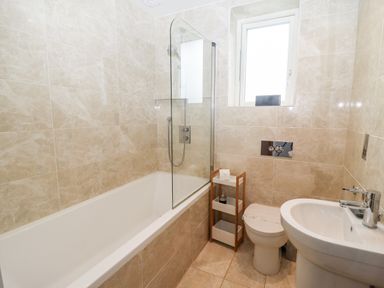 A bathroom with a bathtub shower combo a toilet a sink and a small shelf next to the toilet at 9 Cedars in St Agnes