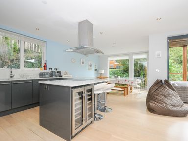 A kitchen with an island counter stools and a dining area with large windows at 9 Cedars in St Agnes
