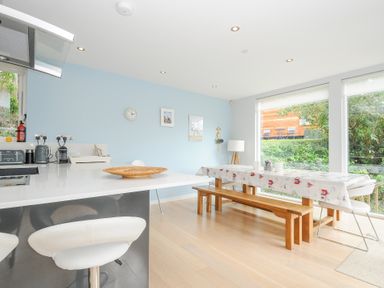 A dining area with a wooden bench and table near large windows and a kitchen counter with stools at 9 Cedars in St Agnes