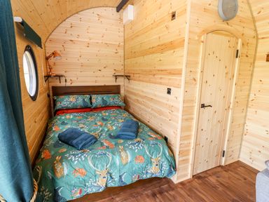 A bedroom with a double bed covered with animal print bedding and two blue towels on top at The Happy Valley Pod in Chipping Norton