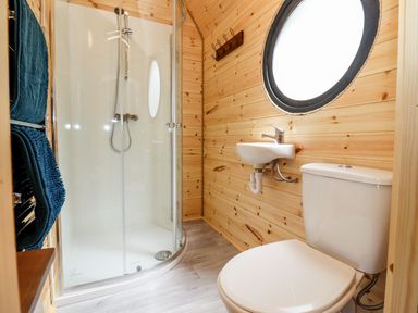 A small bathroom with a toilet sink shower and round window with wooden walls at The Happy Valley Pod in Chipping Norton