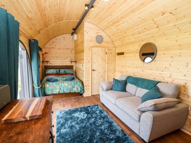 An interior of a wooden pod with a bed, sofa, rug, and curtains at The Happy Valley Pod in Chipping Norton