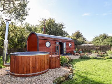 A small wooden cabin with round windows and a hot tub in a garden at The Happy Valley Pod in Chipping Norton