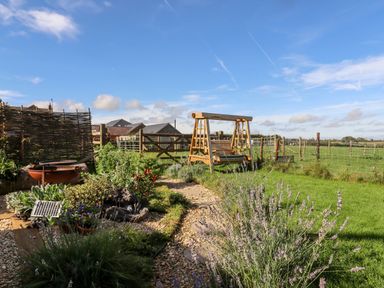 A garden with a wooden swing bench flowers and a fence at The Happy Valley Pod in Chipping Norton