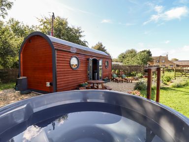 A garden area with a wooden pod cabin lawn chairs picnic table and hot tub at The Happy Valley Pod in Chipping Norton