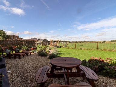 A garden with wooden table and chairs a grassy field and buildings in the background at The Happy Valley Pod in Chipping Norton