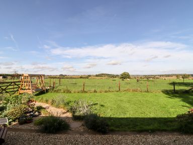 A garden with a wooden swing and grassy field with grazing animals in the background at The Happy Valley Pod in Chipping Norton