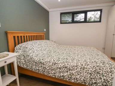 A bedroom with a wooden bed and white nightstand under a window at The Nest in Prestatyn