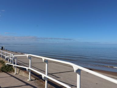 A concrete promenade with white railings overlooking a calm sea with a clear blue sky at The Nest in Prestatyn