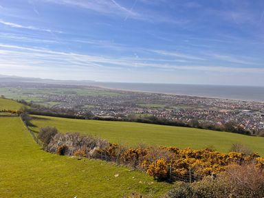 A hillside overlooking a town with houses fields and the sea in the background at The Nest in Prestatyn