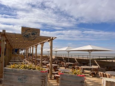 An outdoor seating area with wooden tables and chairs under umbrellas and string lights at The Nest in Prestatyn