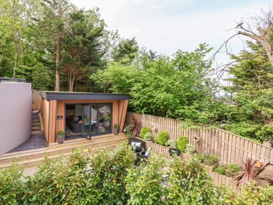A small garden room with glass doors opening to a patio with outdoor seating and plants at The Nest in Prestatyn