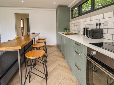 A kitchen with green cabinets stools along a wooden counter and appliances at The Nest in Prestatyn