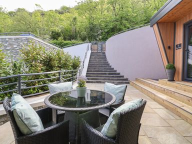 An outdoor patio area with a round glass table and four wicker chairs with cushions at The Nest in Prestatyn