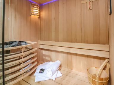 An interior of a wooden sauna with a bench a folded towel and bathrobe a wooden bucket with a ladle and a wall light at The Nest in Prestatyn