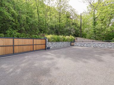 A driveway with a wooden gate and stone wall surrounded by trees at The Nest in Prestatyn