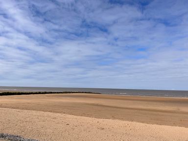A sandy beach with a stone breakwater and the sea under a cloudy sky at The Nest in Prestatyn