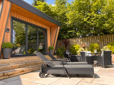 An outdoor patio with lounge chairs table chairs grill and potted plants at The Nest in Prestatyn
