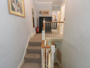 A hallway with stairs and framed artwork at Longmoor, Tenby