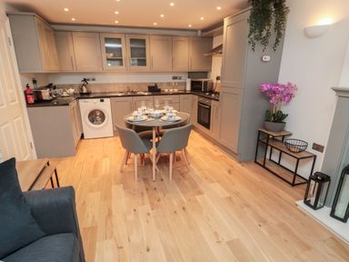 A kitchen with gray cabinets wooden floor round dining table with four chairs and a washing machine at Lavenna in Alnwick