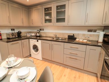 A kitchen with grey cabinets and black countertops featuring a washing machine toaster kettle and a dining table at Lavenna in Alnwick