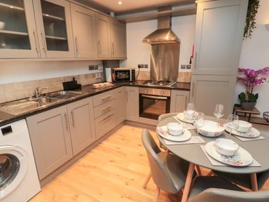 A kitchen with grey cabinets a dining table set with floral dishes and a washing machine at Lavenna in Alnwick