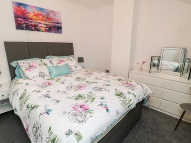 A bedroom with a bed with floral bedding a dresser with a mirror and a painting on the wall at Lavenna in Alnwick