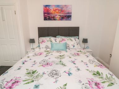 A bedroom with a floral bedspread on the bed two bedside tables with lamps and a colorful painting above the bed at Lavenna in Alnwick