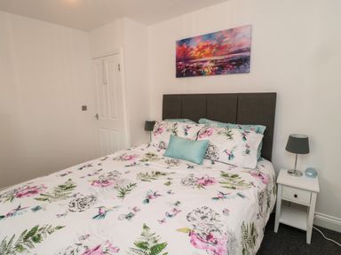 A bedroom with a bed that has floral bedding and pillows a bedside table with a lamp and clock and a colorful painting above the bed at Lavenna in Alnwick