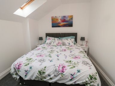 A bedroom with a bed covered in floral and bird patterned bedding two bedside tables with lamps and a skylight window at Lavenna in Alnwick