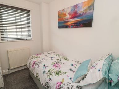 A bedroom with a single bed with floral bedding a window with blinds a radiator and a colorful painting on the wall at Lavenna in Alnwick