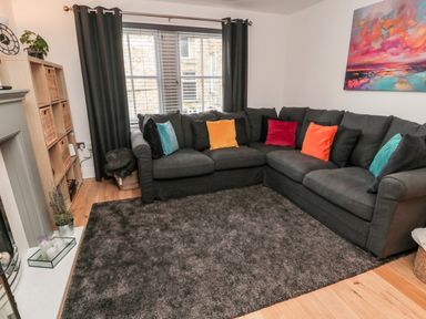 A living room with a dark gray corner sofa with colorful cushions a gray rug a wooden floor and a shelf with wicker baskets at Lavenna in Alnwick