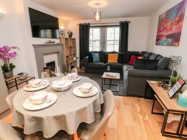 A living room and dining area with a round table set for four and a sectional sofa with colorful cushions at Lavenna in Alnwick