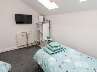 A bedroom with a bed covered in blue floral bedding folded towels on the bed a wall-mounted television and a white shelving unit under a skylight at Lavenna in Alnwick