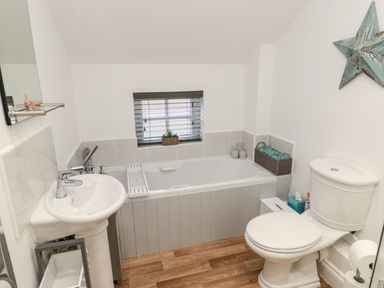 A bathroom with a bathtub sink toilet wooden floor and a small window at Lavenna in Alnwick