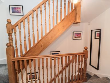 A wooden staircase with framed pictures on white walls and a wall mirror at Lavenna in Alnwick