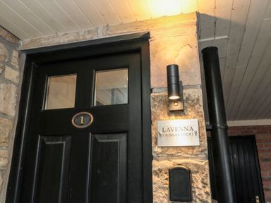 A black door with the number 1 next to a stone wall with a light fixture and a sign reading Lavenna 1 Jubilee Court at Lavenna in Alnwick